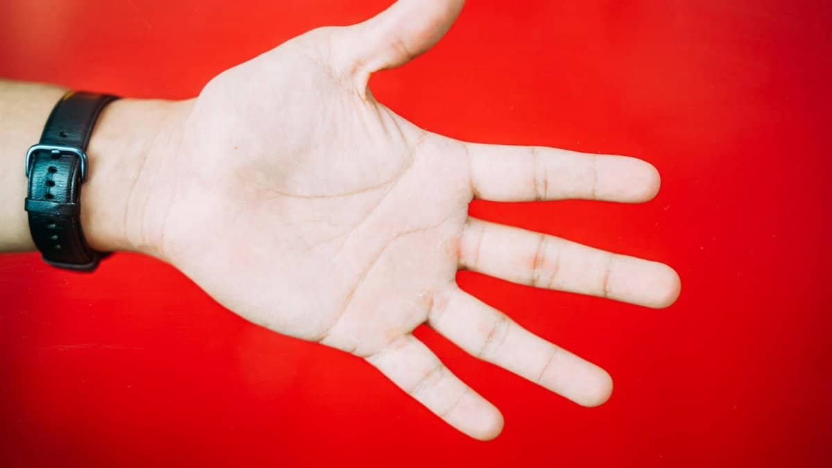 A close-up view of an outstretched hand with a black watch against a vibrant red backdrop.
