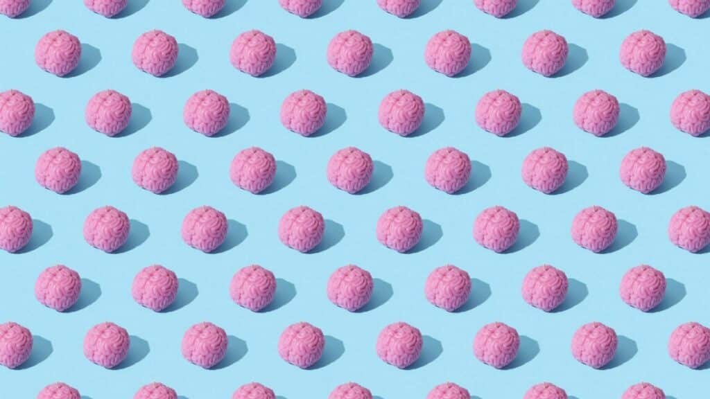 Creative composition of pink brain models in a repeating pattern on a light blue surface, showcasing abstract thinking.