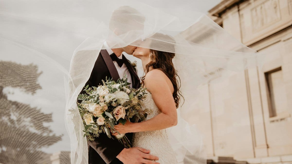 Bride and groom share a tender kiss under a veil, showcasing love and romance on their special day.