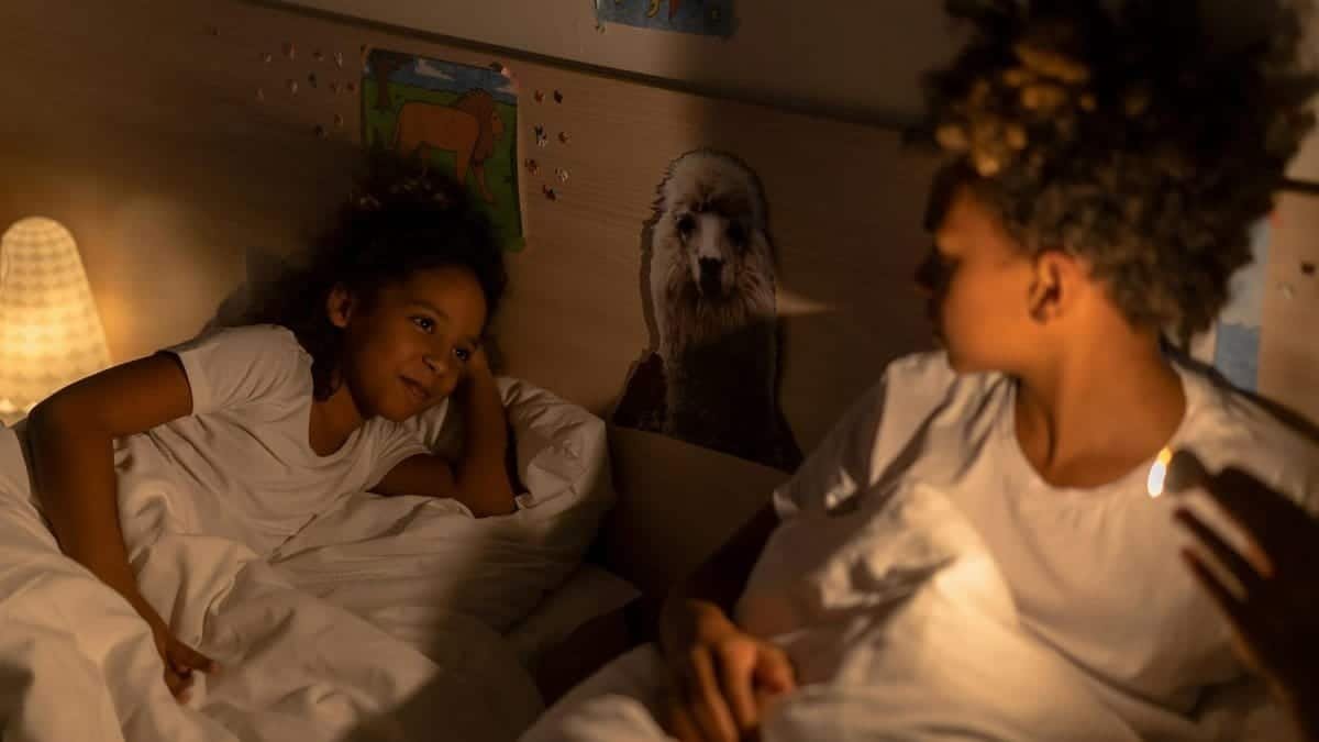 Two siblings sharing a quiet bedtime moment in a softly lit bedroom.