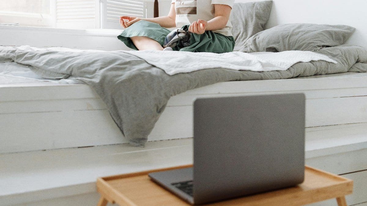 Woman practicing meditation on bed by window, embracing tranquility indoors. via Pexels