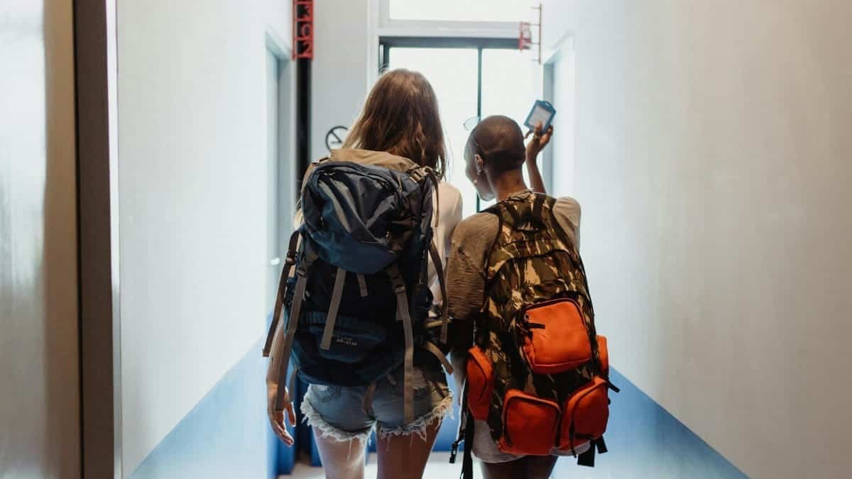 Two women with backpacks walking through a hallway, suggesting travel friendship.