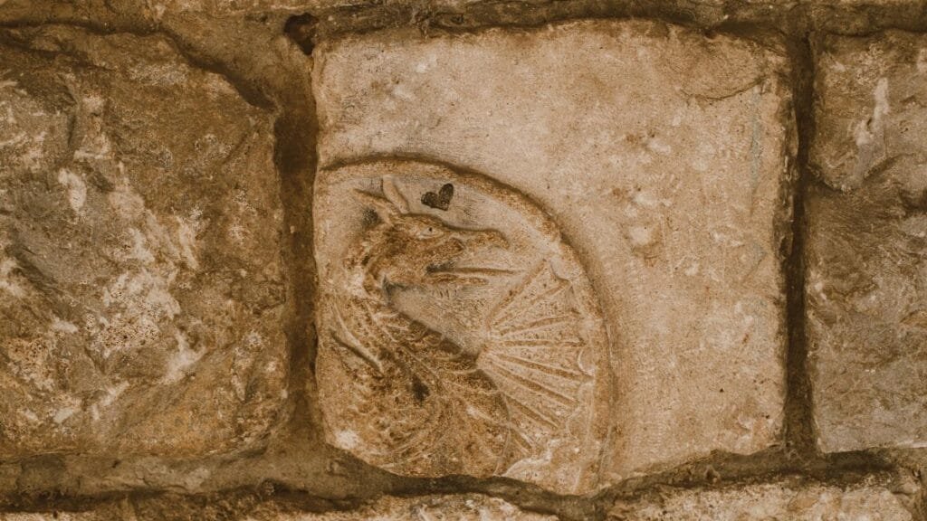 Close-up of an ancient dragon carving on textured stone, suggesting historical mystery.