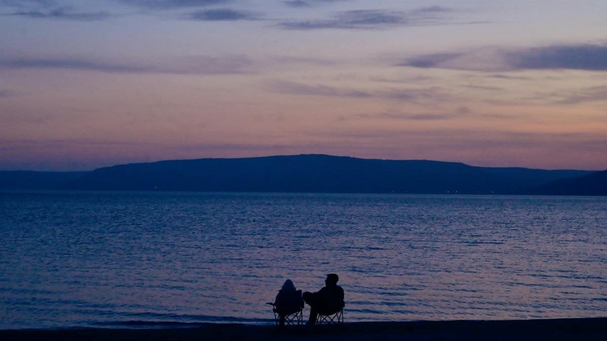 A couple enjoys a serene seaside sunset in Çanakkale, Türkiye, creating an atmosphere of evening tranquility.