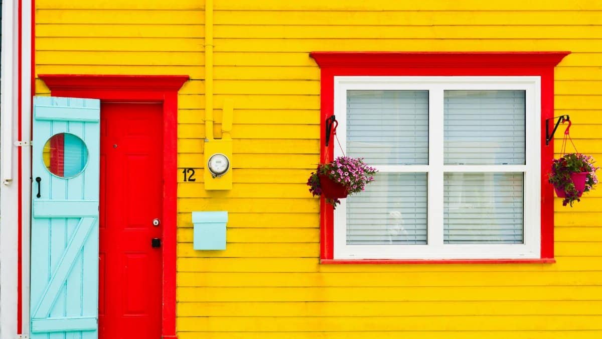 Colorful yellow house with red door and window frames in a lively street in St. John's, Canada.
