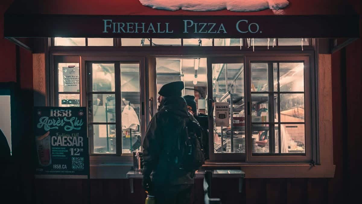 A customer waits at the Firehall Pizza Co window during a winter evening.