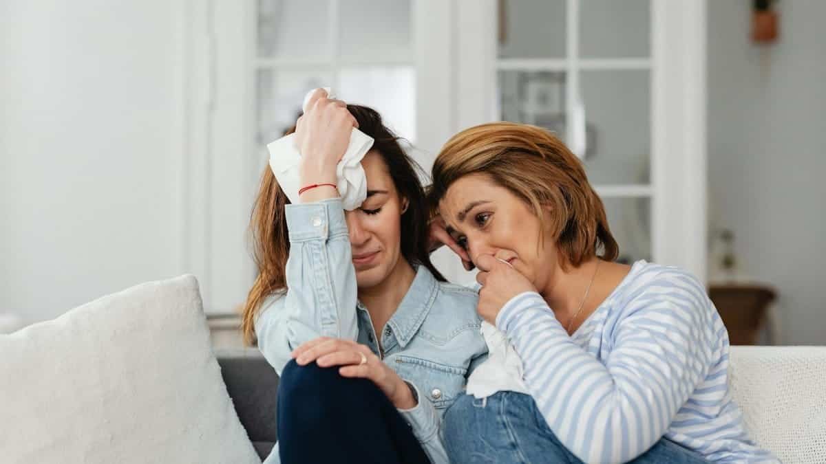 Two women sitting on a sofa, comforting each other in a moment of shared emotions.