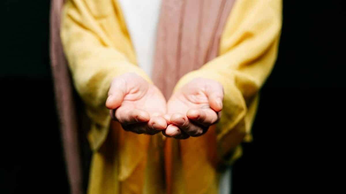 A person in a yellow garment extends open hands in a gesture of offering or invitation.