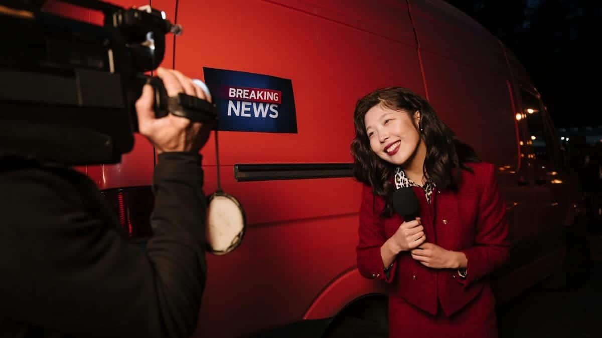 Asian female reporter in a red blazer reporting live on the news outdoors in the evening.