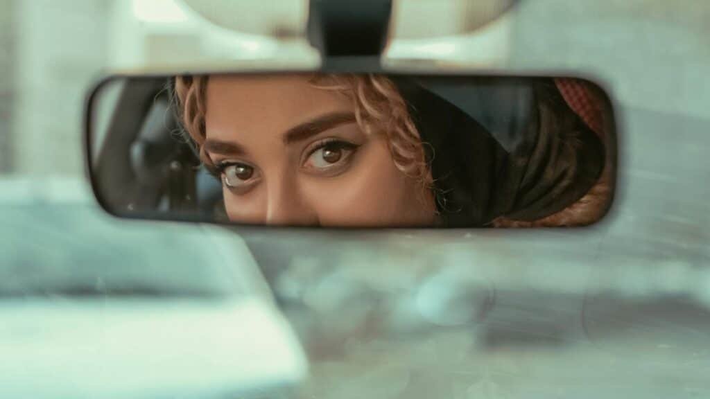 Close-up of woman's eyes in rearview mirror, conveying mystery and contemplation.