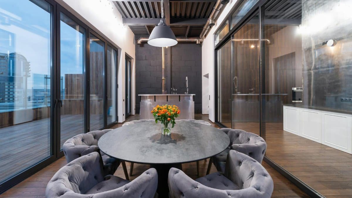 Interior of modern lounge zone with round table and comfortable armchairs placed near panoramic windows in evening time