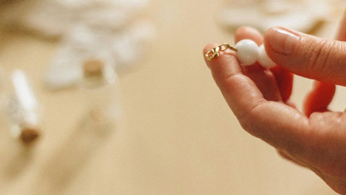 Close-up of hands crafting jewelry with delicate white beads and gold accents.
