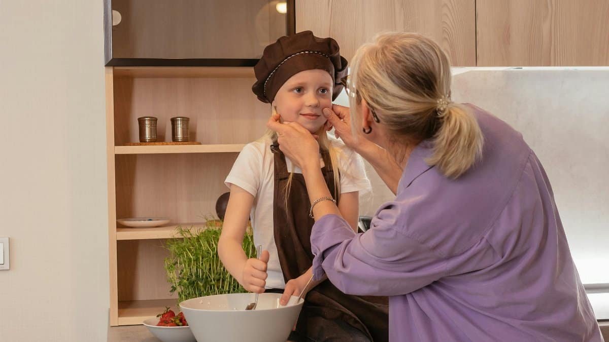An elderly woman and her grandchild share a joyful moment cooking in the kitchen together.
