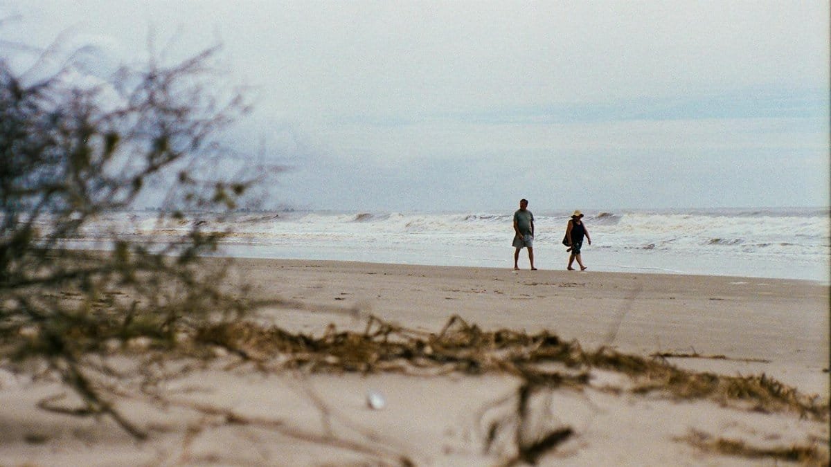 A peaceful scene with two people walking along a sandy beach by the ocean during summer.