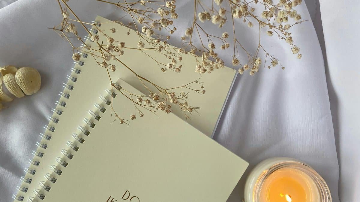 Top view composition of white spiral copybooks with inscription Do What You Want placed on white cloth with burning candle and tender flower