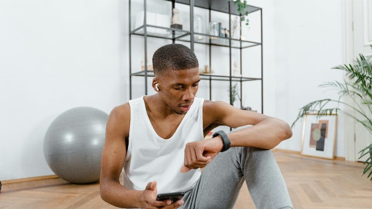 Young man in active wear resting indoors, checking smartwatch after a workout session.