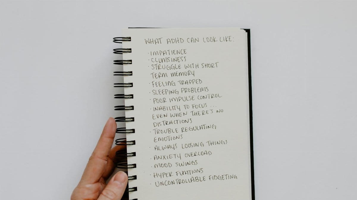 Handwritten list of ADHD symptoms on a notepad held by a person.