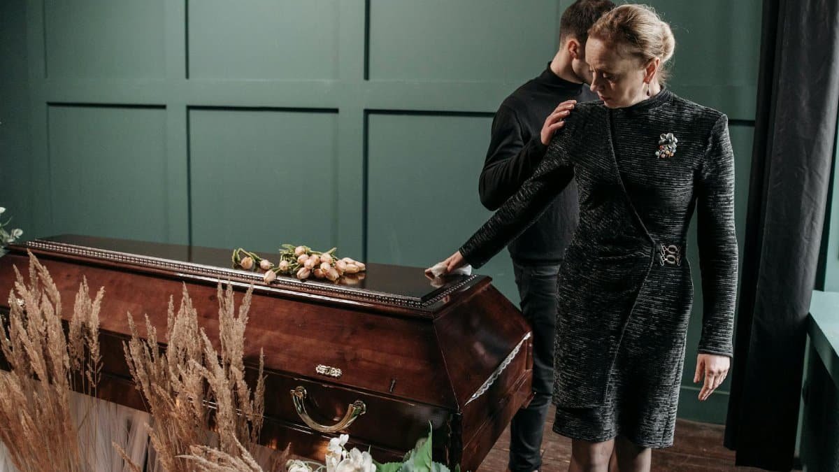 A solemn moment at a funeral with family mourning beside a coffin indoors.