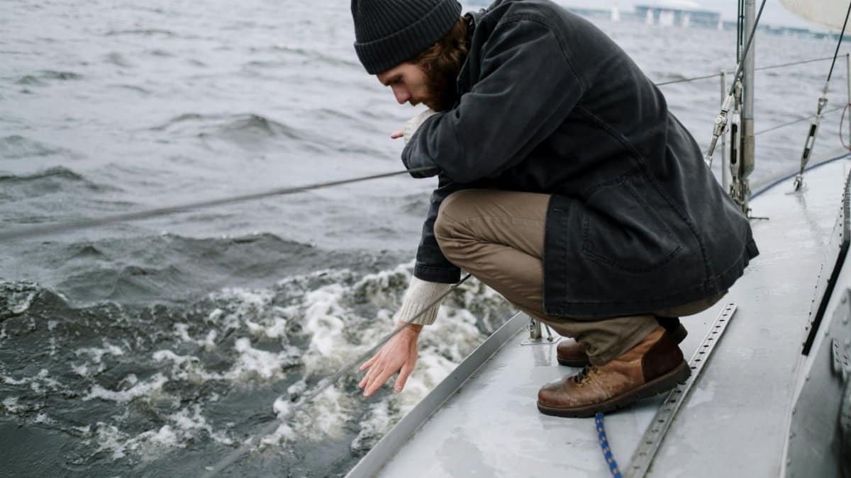 A thoughtful sailor crouches aboard a yacht on a cloudy day.