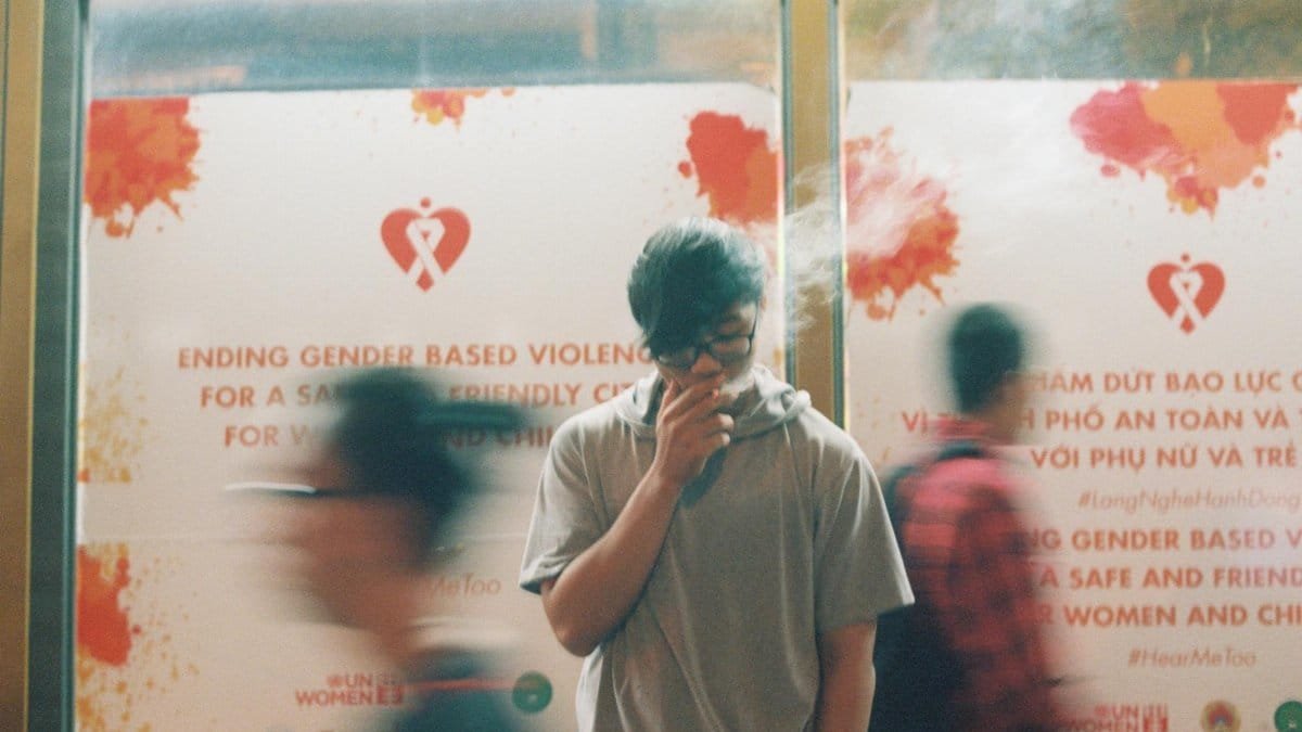 Man smoking in front of an anti-gender violence poster in Vietnam.