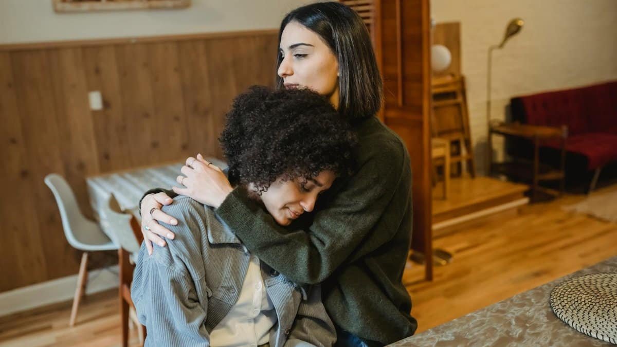 A heartfelt moment of support and empathy between two young women sharing an embrace indoors.