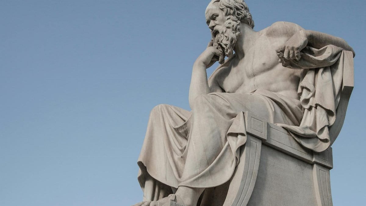 Stone statue of philosopher Socrates sitting in thoughtful pose in Athens, Greece under a clear blue sky.
