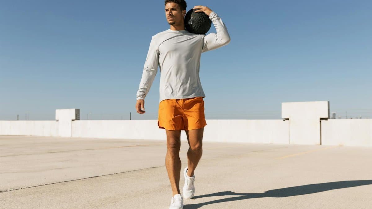 Man in orange shorts exercises with a medicine ball on a sunny Austin rooftop.