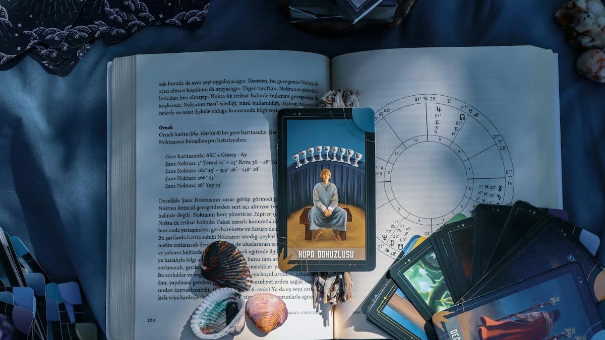 An artistic flat lay of tarot cards and astrology on a book with seashells, featuring Kupa Dokuzlusu card.