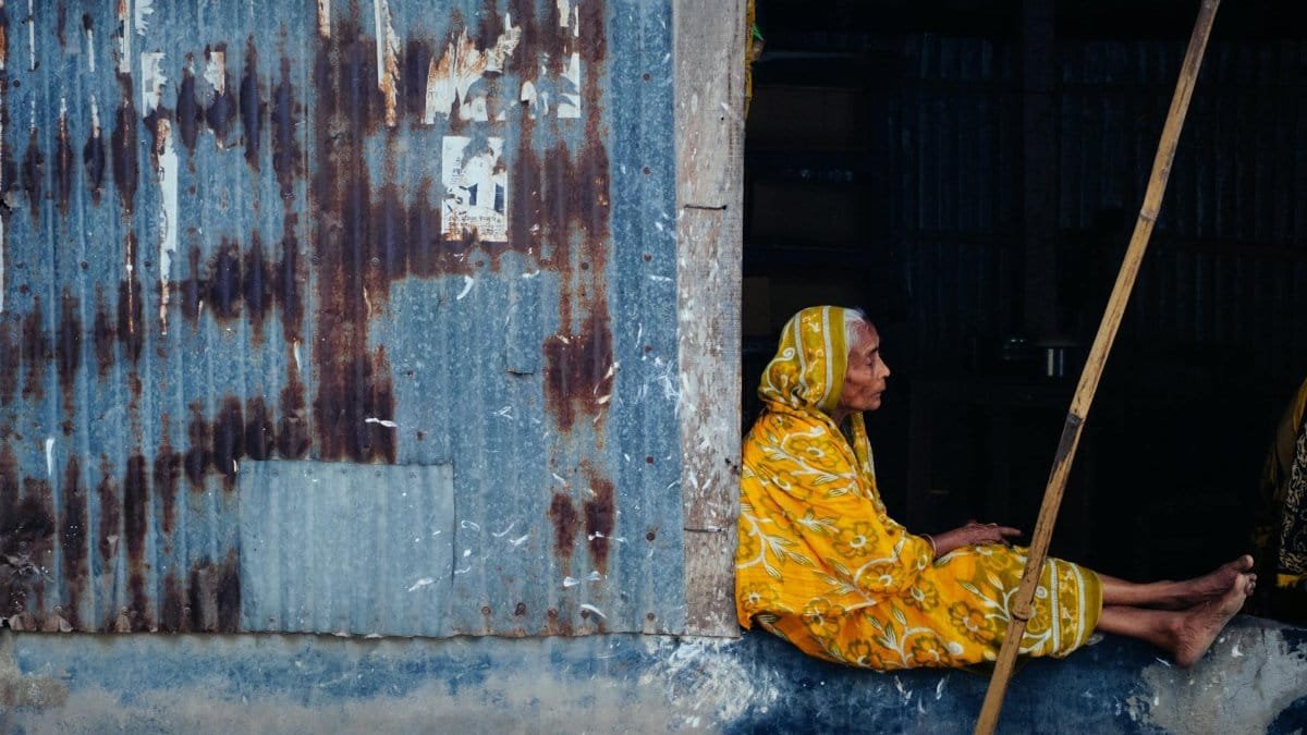 Elderly woman sitting in a doorway in Chilmari, Bangladesh, showcasing cultural heritage.