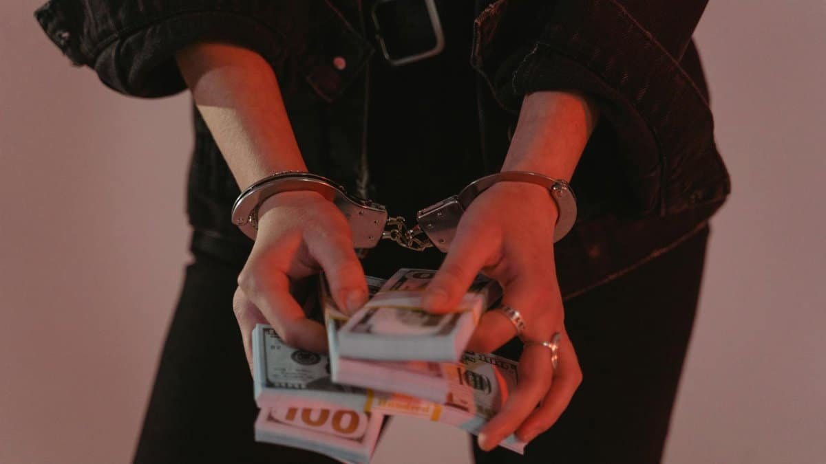 Close-up of hands holding cash with handcuffs, symbolizing crime and punishment.
