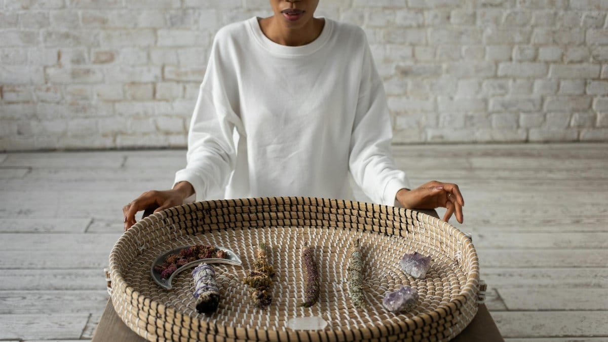 A woman displays a basket containing crystals and sage, enhancing a spiritual atmosphere.