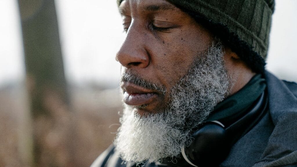 Closeup of bearded concentrated African American male with headphones on neck meditating with closed eyes