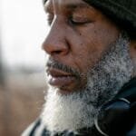 Closeup of bearded concentrated African American male with headphones on neck meditating with closed eyes