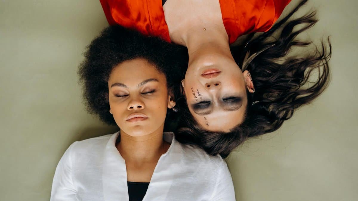 Two women in meditation pose lying head-to-head, embodying peace and spirituality.