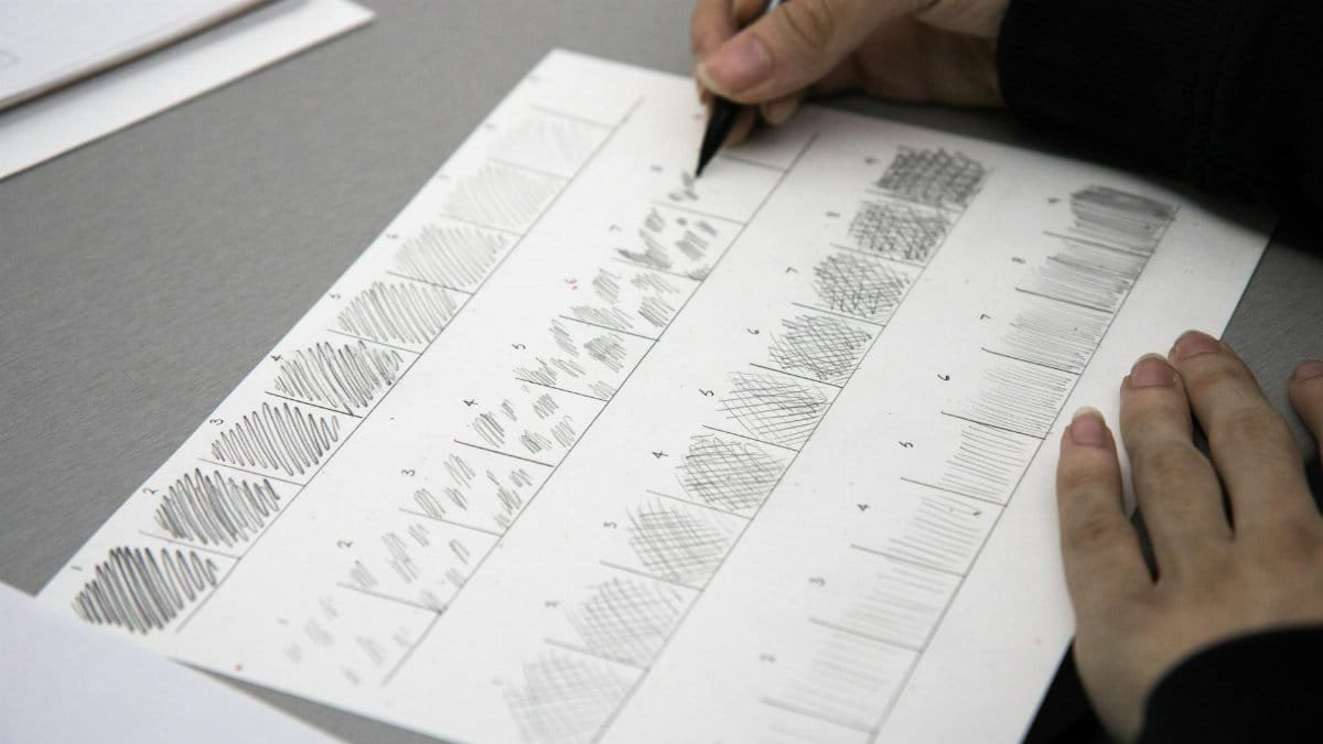 Close-up photo of hands using a pen to practice shading techniques on paper.