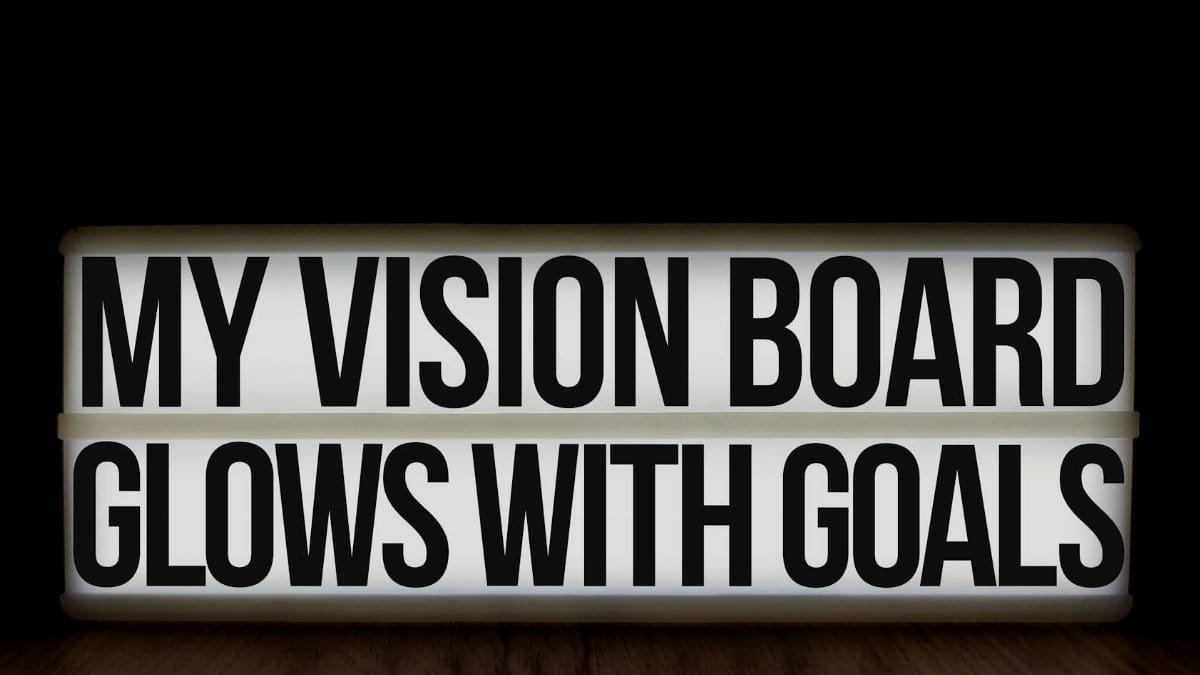 A glowing lightbox displaying the motivational message 'My Vision Board Glows With Goals' on a wooden surface.