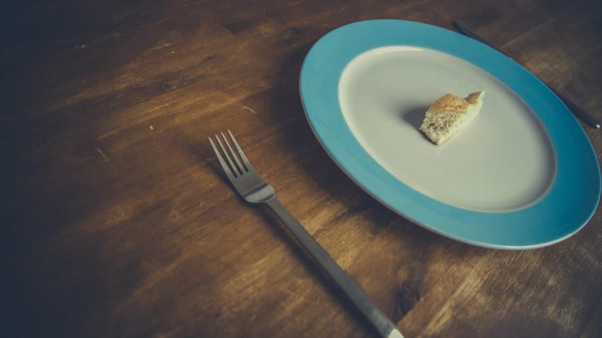 Minimalist bread piece on a blue-rimmed plate with fork and knife on wooden table.