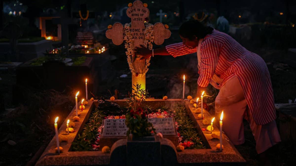 A woman arranging candles at a grave during a nighttime candlelit vigil, honoring tradition.
