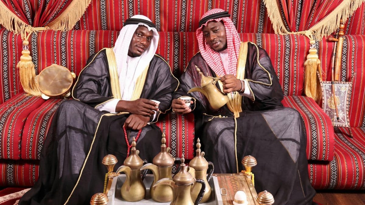 Two men in traditional attire enjoy a tea ceremony indoors, reflecting cultural heritage.