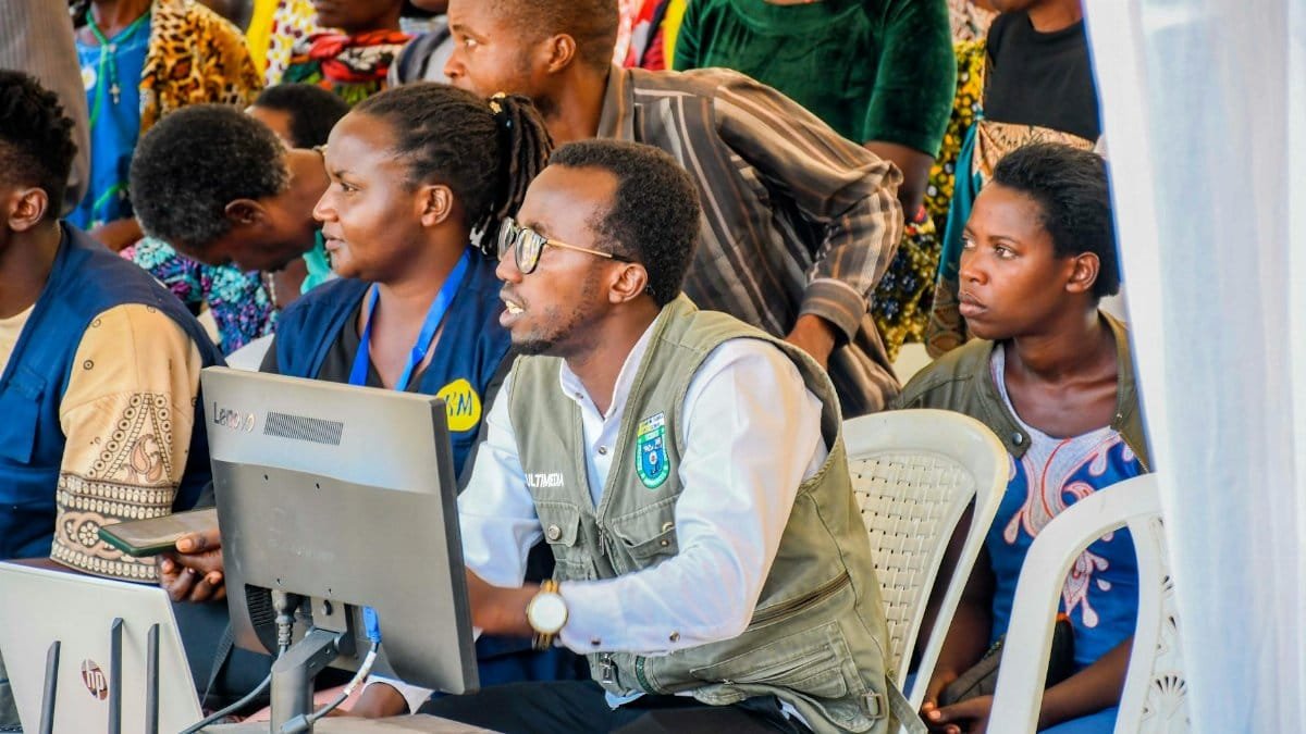 A diverse group of adults engaging with technology at a community event in Rwanda.