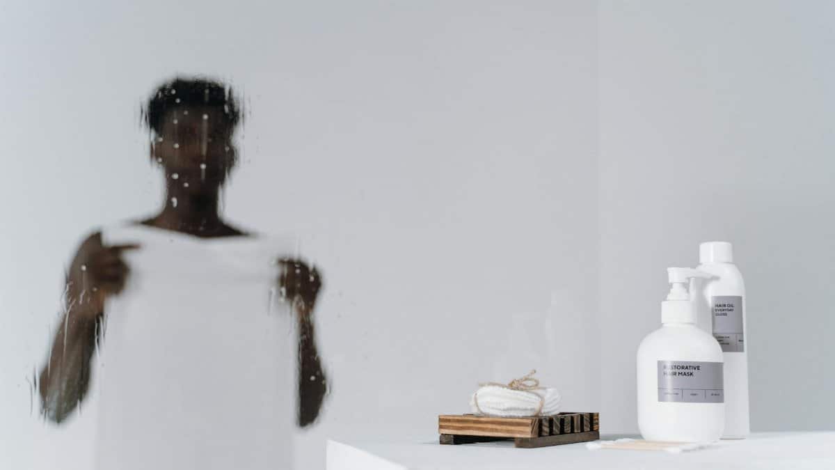 Blurred reflection of a man with skincare bottles on a white background.
