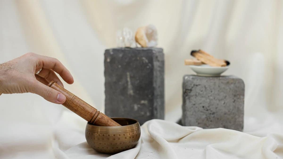 Serene setup with singing bowl, Palo Santo, crystal, and hand for meditation or relaxation ambiance.