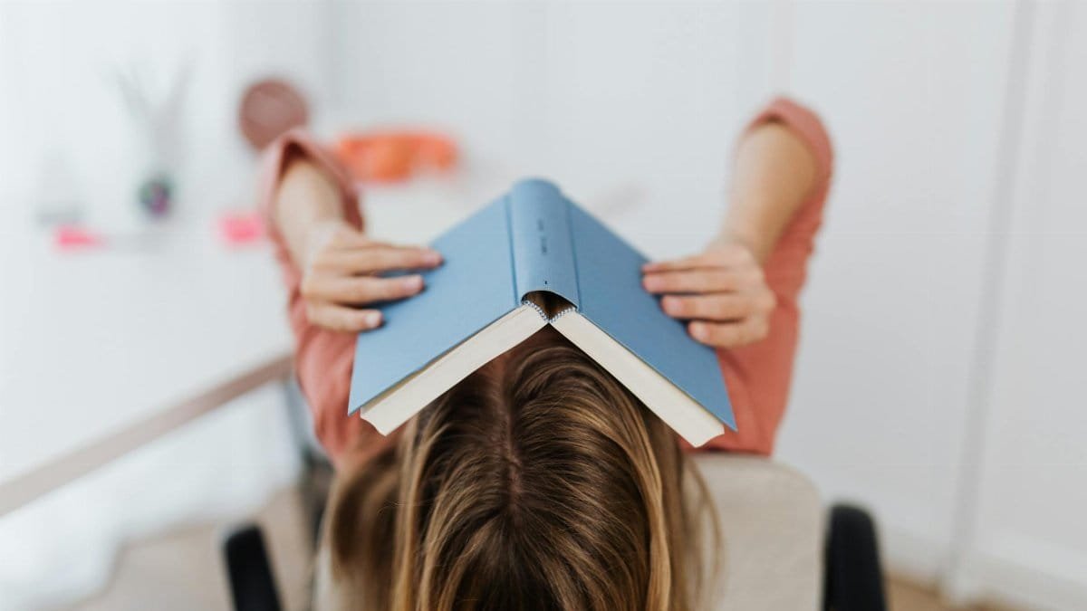 Adult woman covering face with a book in an indoor setting, showcasing study stress.
