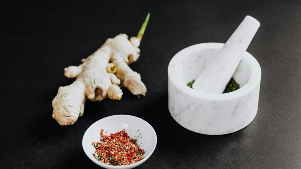 A culinary scene featuring a mortar with spices and ginger root on a black background.