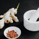 A culinary scene featuring a mortar with spices and ginger root on a black background.