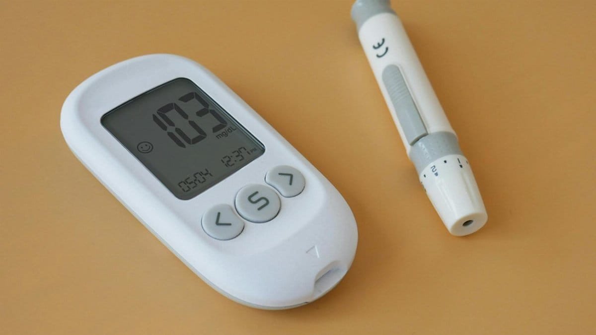 Close-up of a digital blood glucose meter and lancet pen on a brown surface.