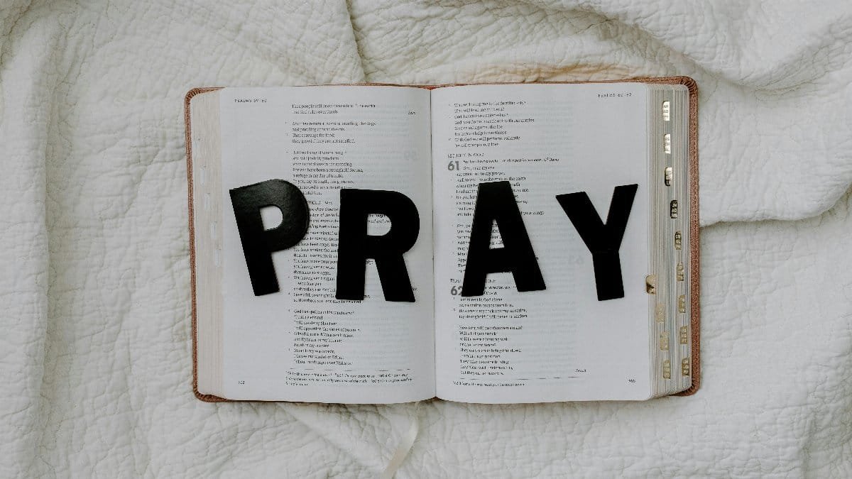Open Bible with black letters spelling 'PRAY' on a white quilted fabric background.
