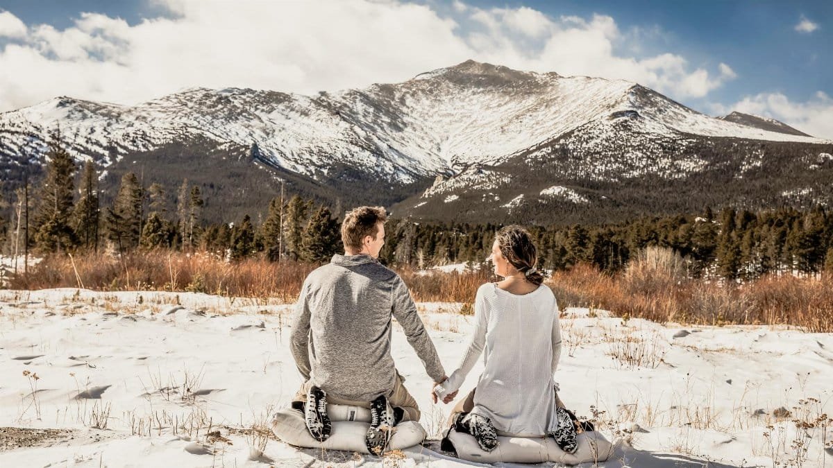 Couple sitting in snow, facing a scenic mountain view in Colorado, USA.