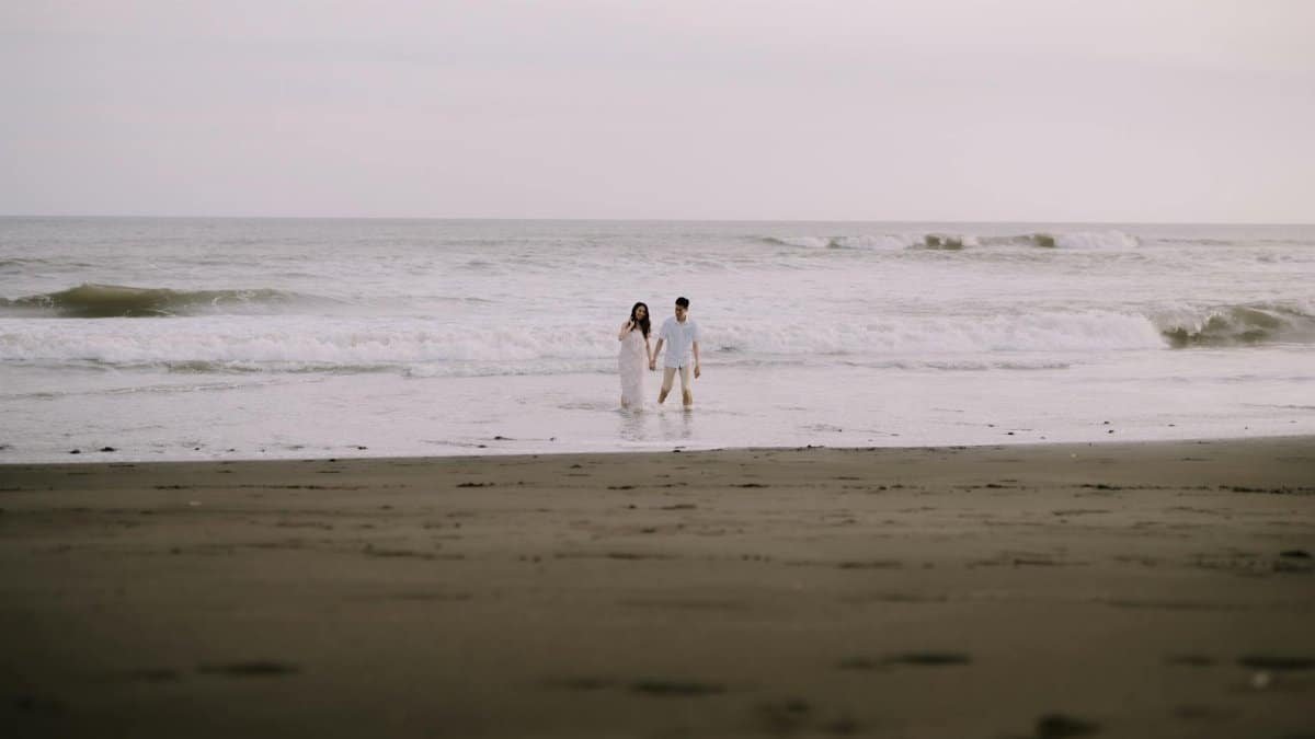 A couple walks hand in hand on a serene Indonesian beach during their pre-wedding photoshoot.