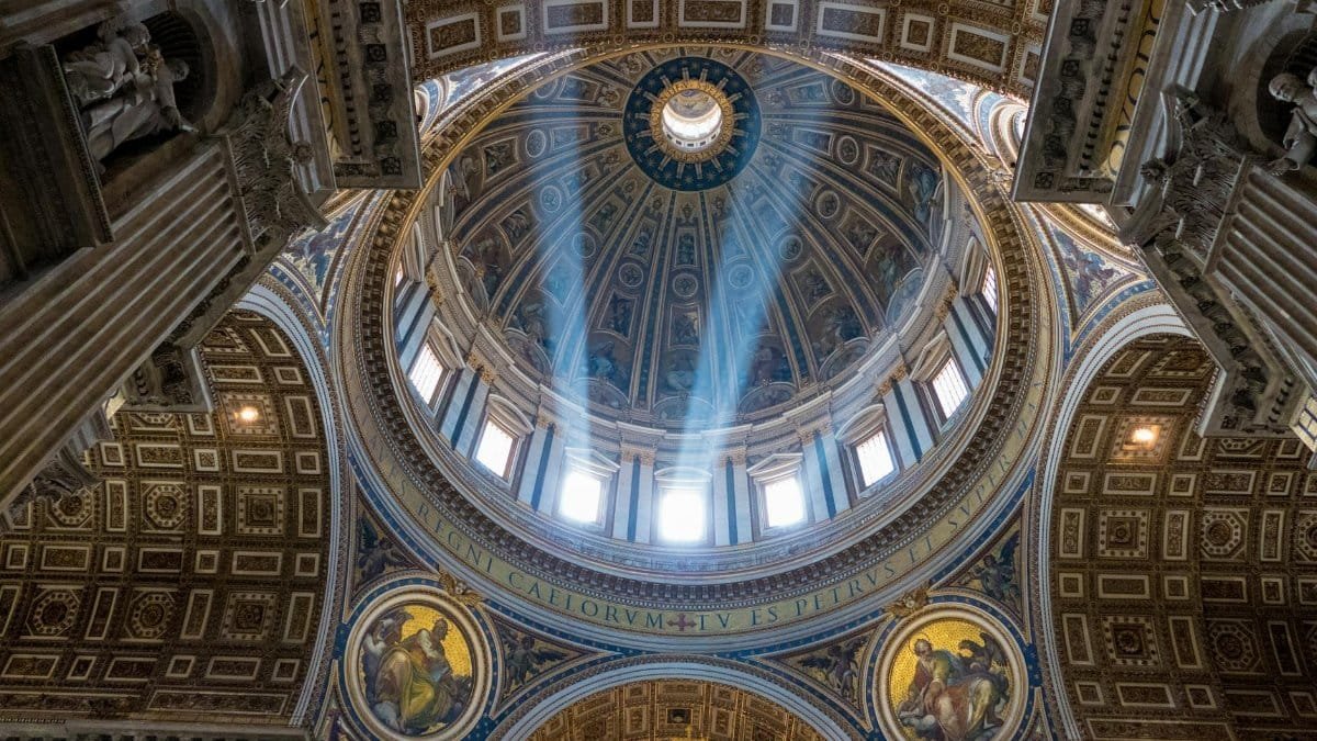 Sunlight streams through the dome of St. Peter's Basilica, revealing intricate frescoes and architecture in Vatican City.